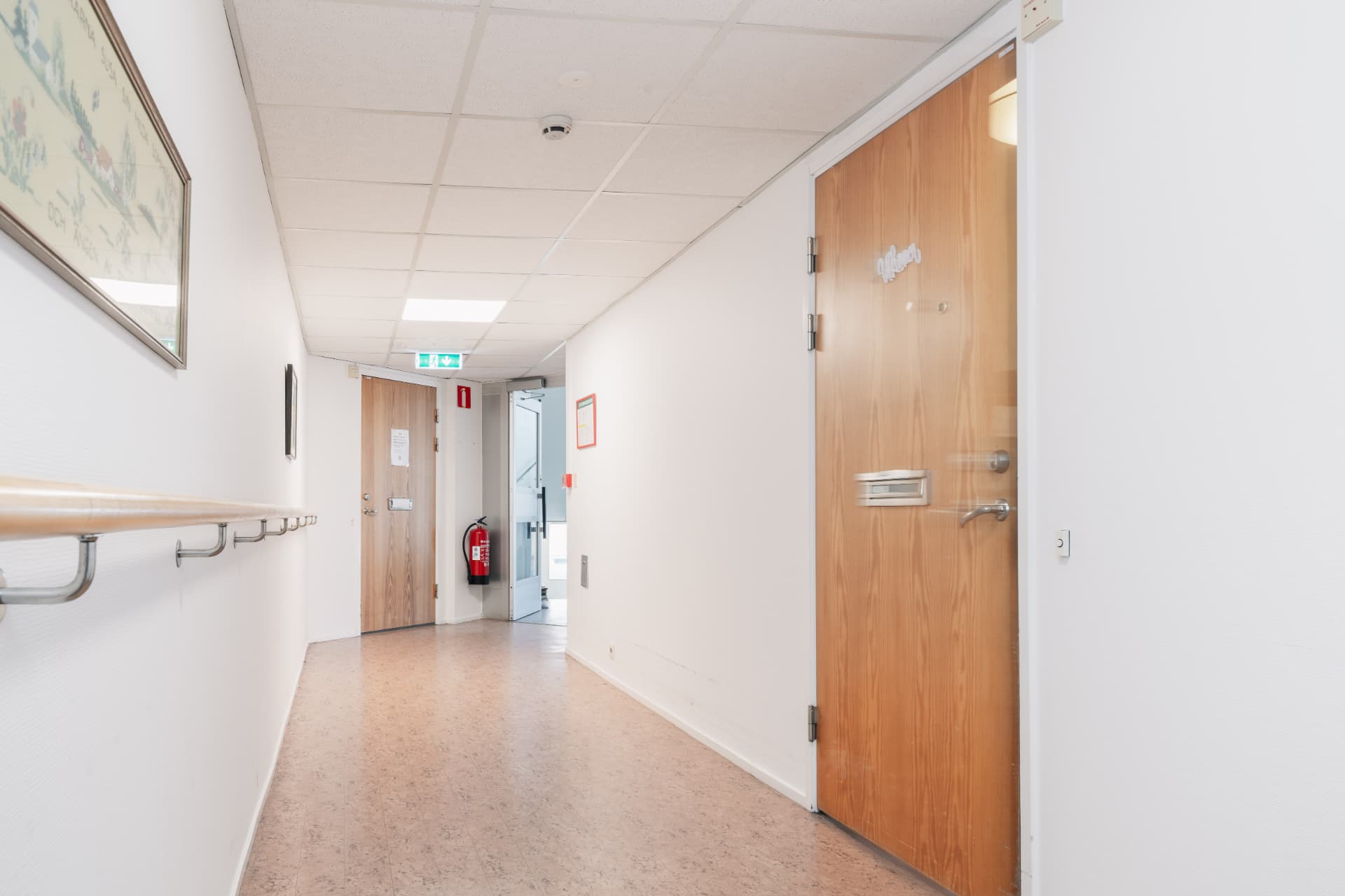 Korridor med lägenhetsdörrar, ledstång och utgång mot trapphuset