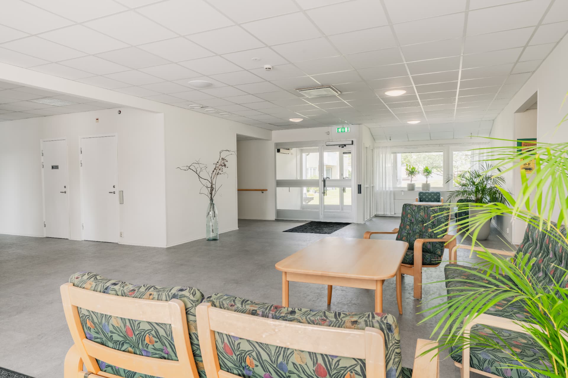 Foajé med sittgrupper, växter och entrédörrar ut mot gården